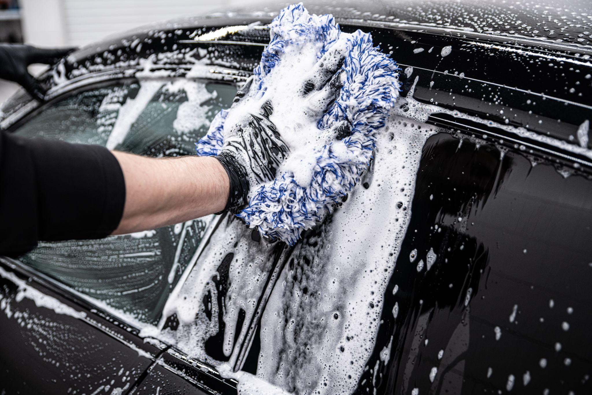 Professional hand washing a black vehicle with a microfiber wash mitt during a mobile detailing service in San Diego.